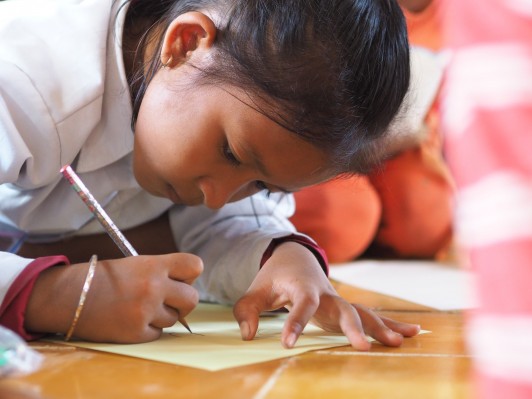 私たちが届けた日本製の鉛筆とノートで真剣に絵を書く女の子。 