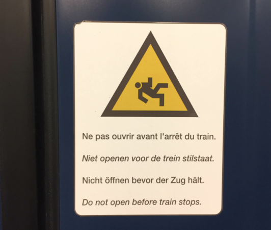上からフランス語、オランダ語、ドイツ語、英語で「電車が停車するまでドアを開けないでください。」多言語国家ならではの電車の注意書き。
